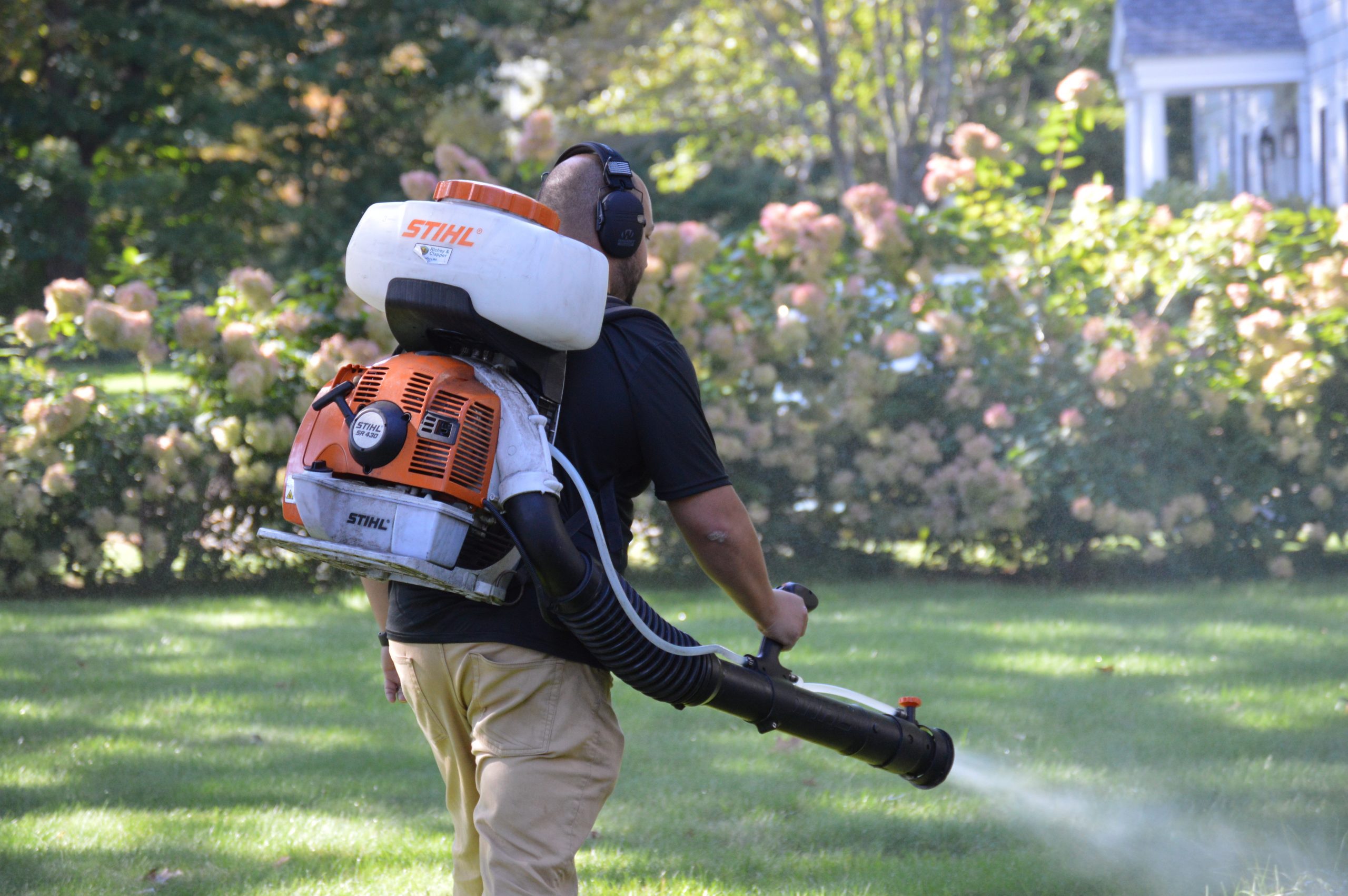 Professional tick and mosquito technician spraying a yard for pests using a backpack sprayer