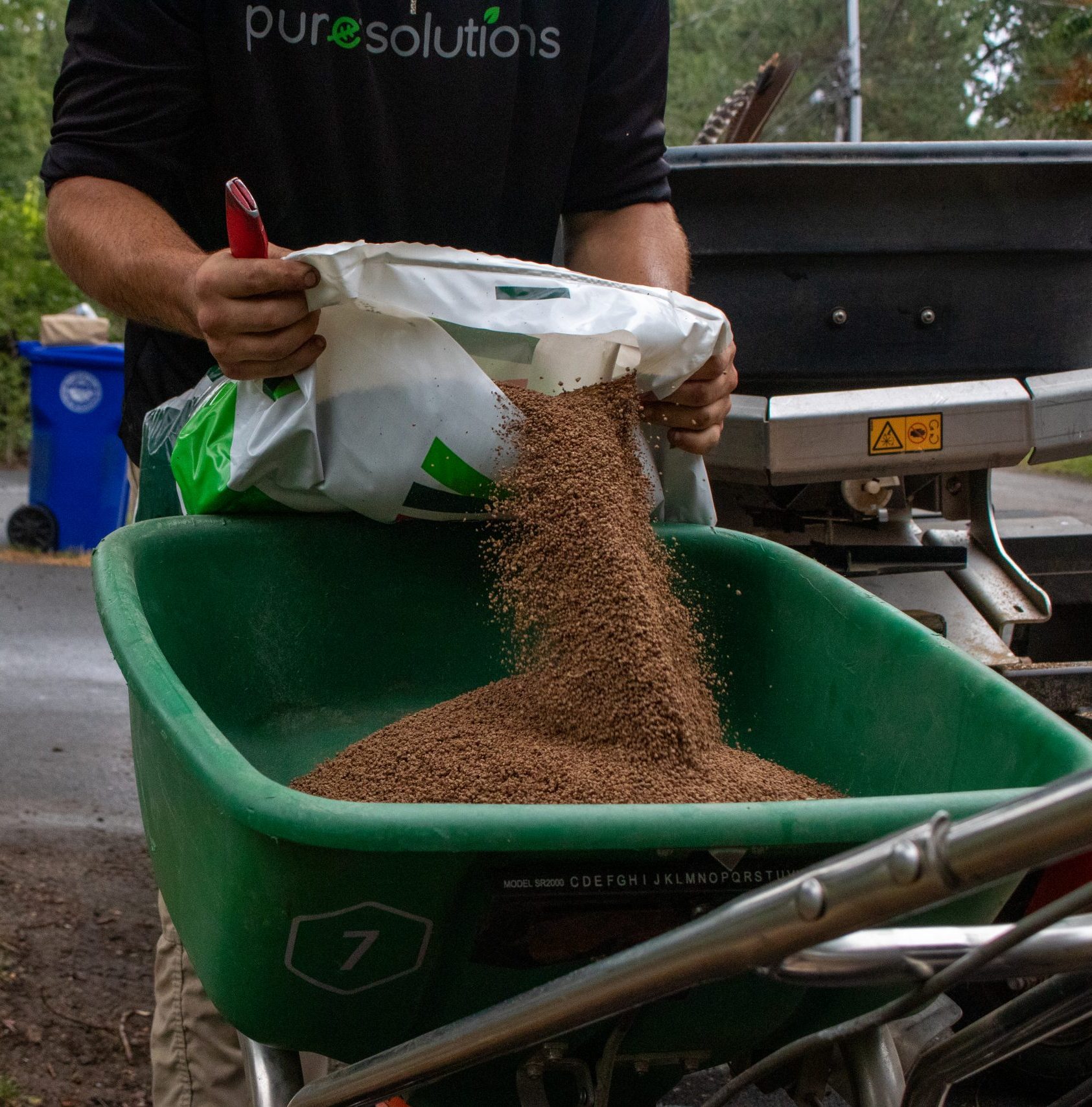 A Pure Solutions pours organic fertilizer into a spreader. 